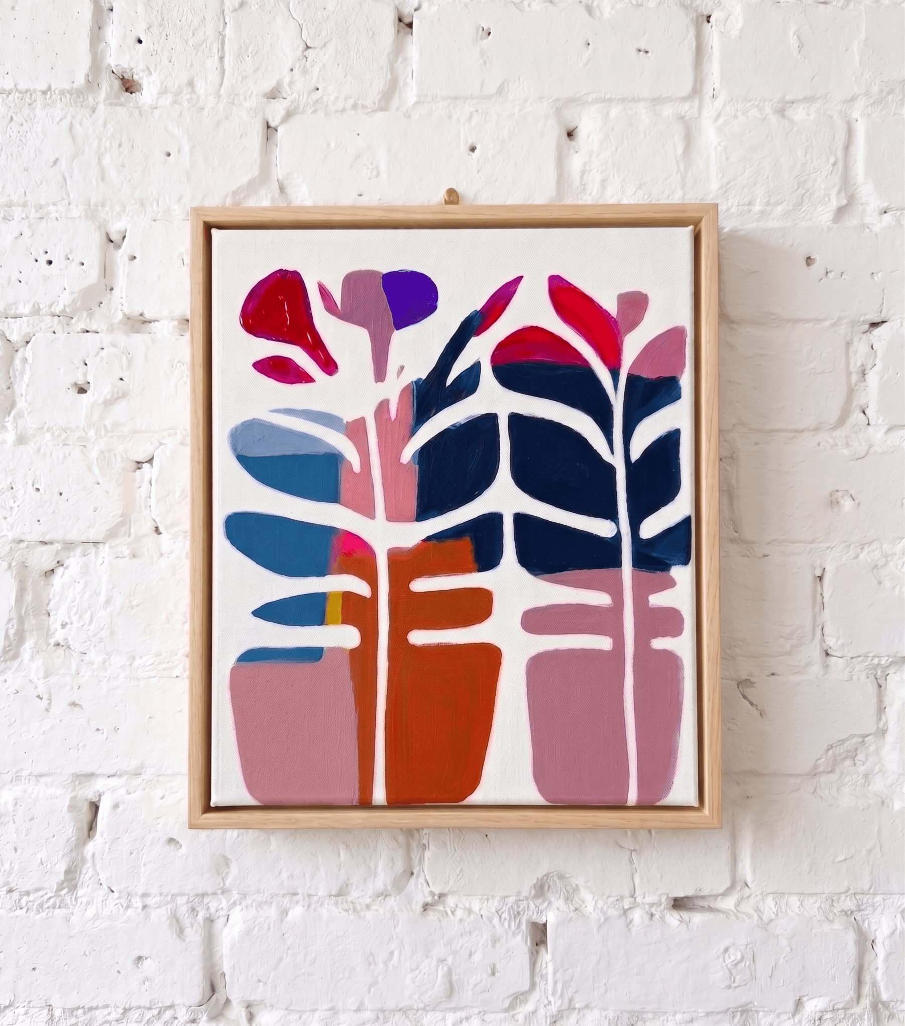 A framed Smudge canvas on the studio brick wall: bold botanicals painted over to reveal layered colour underneath