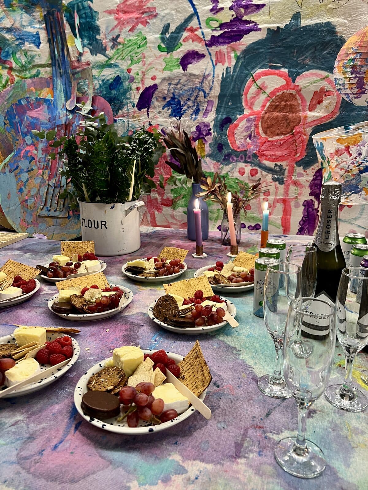 The table set for an adult workshop at Smudge Artspace, plates of cheese and fruit and lit candles on the painted cloth